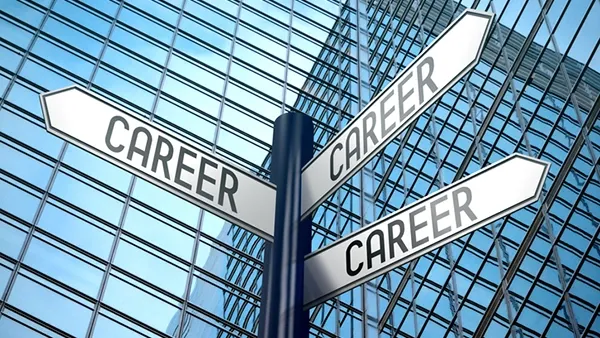Photo of a signpost with three directional arrows labeled “CAREER” in front of a modern glass office building, symbolizing career choices.
